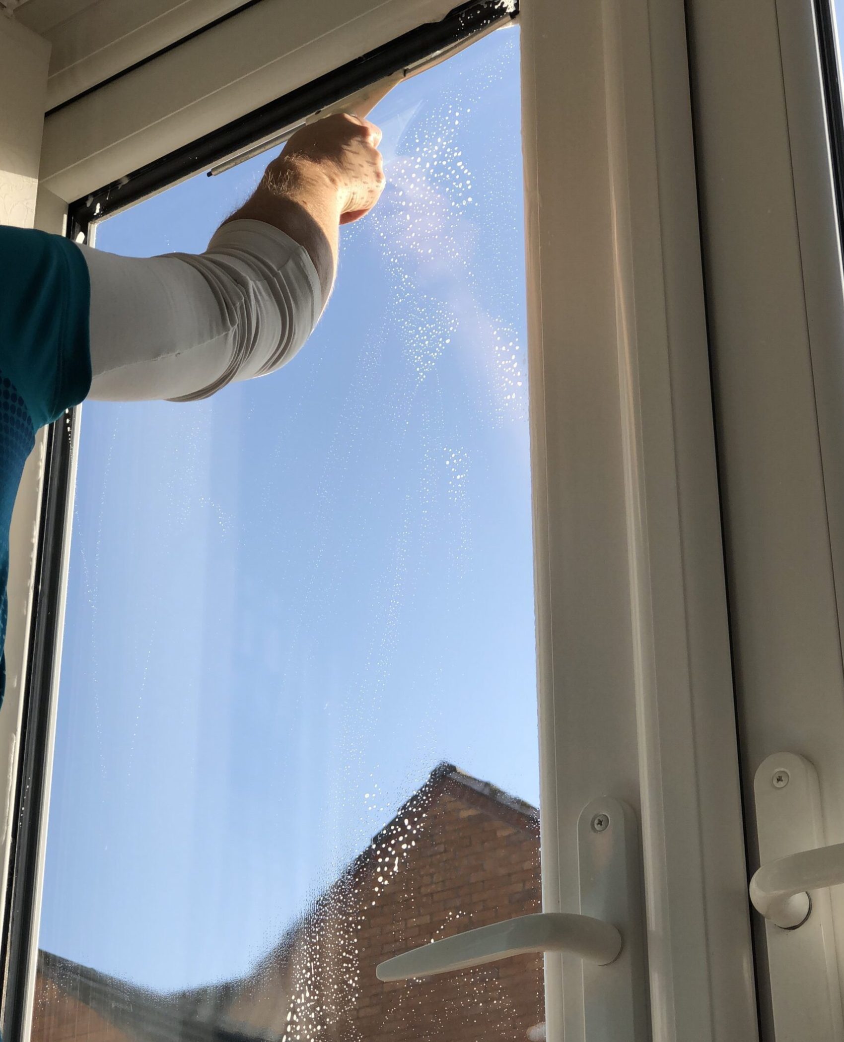 Fensterreinigung in Hannover: Mann reinigt Fenster mit Wischer und Sprühflasche.